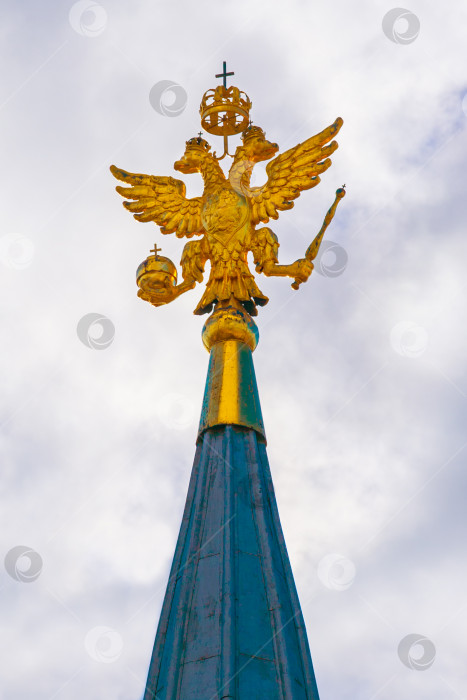 Скачать Золотой герб Российской Федерации с двуглавым орлом на вершине Кремлевской башни на фоне серого пасмурного неба фотосток Ozero