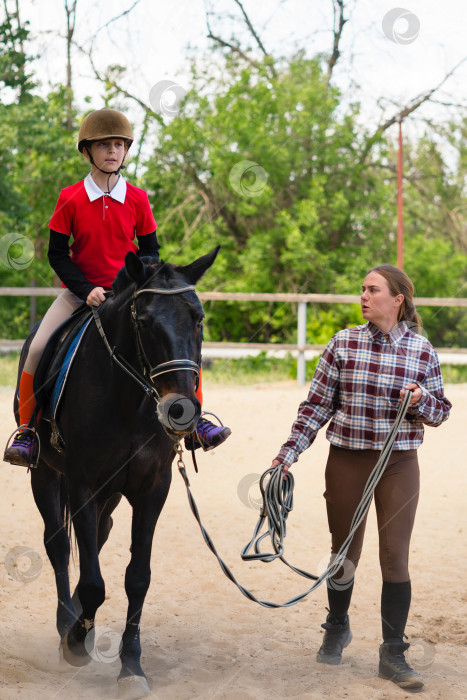 Скачать Инструктор ведет юного наездника верхом на лошади на тренировке. фотосток Ozero