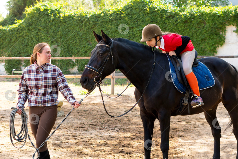 Скачать Инструктор обучает юного наездника обращению с лошадью на манеже для верховой езды. фотосток Ozero