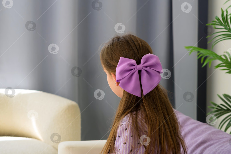 Скачать Девушка с фиолетовым бантом в волосах сидит у окна. фотосток Ozero