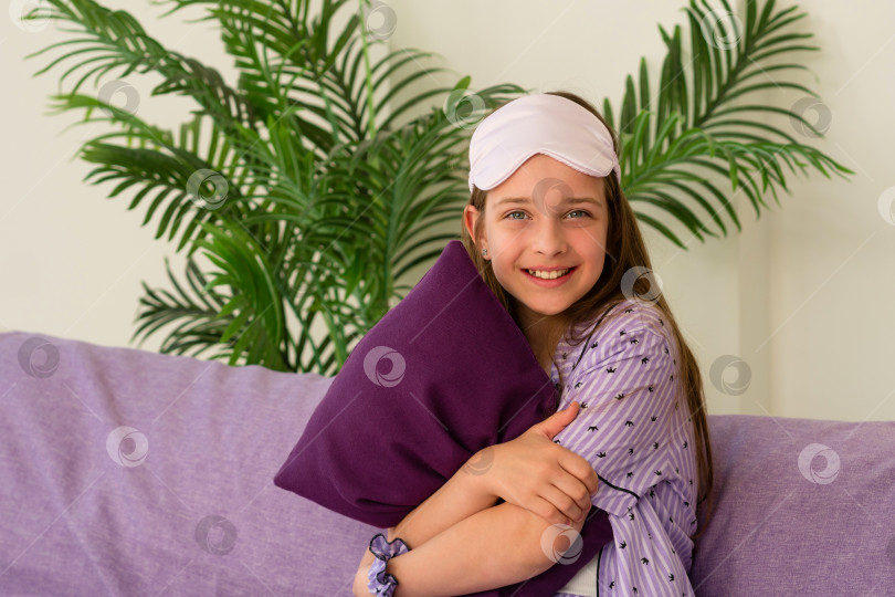 Скачать Счастливая девушка обнимает подушку, сидя на фиолетовом диване фотосток Ozero