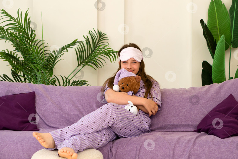 Скачать Девушка обнимает плюшевого мишку на диване в маске для сна. фотосток Ozero