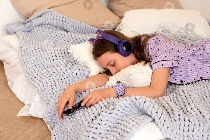 Скачать Девочка-подросток спит в постели с наушниками и смартфоном. фотосток Ozero