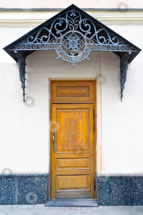Скачать Вид на крыльцо с коричневой деревянной дверью и кованой декоративной решеткой на фронтоне фотосток Ozero