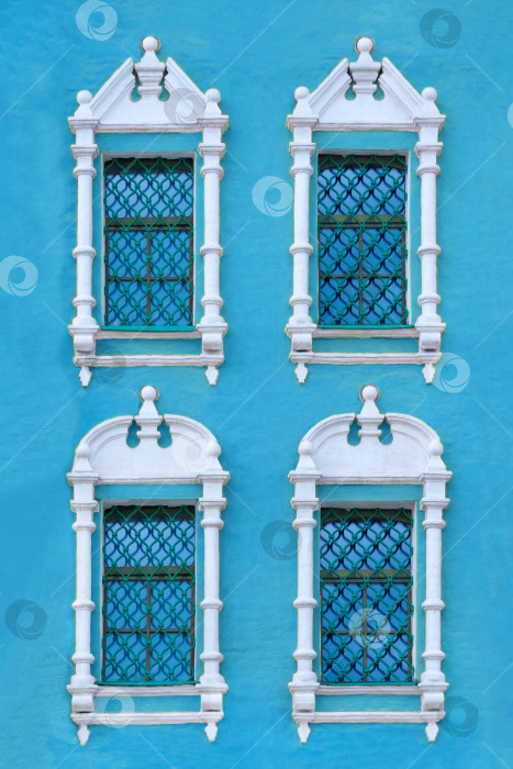 Скачать Вид крупным планом на фасад старинного голубого здания с четырьмя окнами с резными наличниками из белого камня в качестве текстуры (вертикальная ориентация) фотосток Ozero