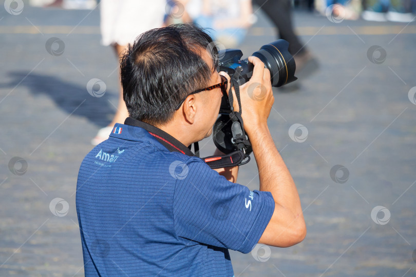 Скачать Москва, Россия, август 2018 года: Турист из Азии фотографирует на зеркальную камеру на Красной площади (редакционная статья) фотосток Ozero