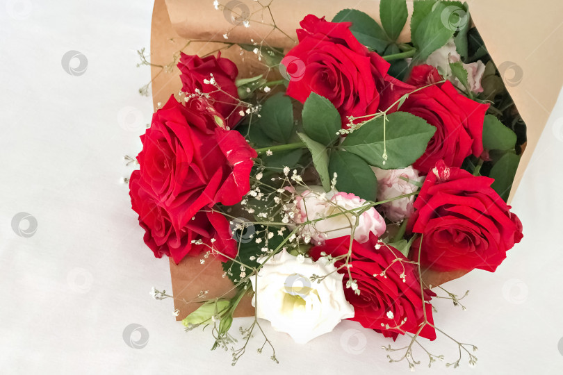 Скачать Красные розы, завернутые в коричневую крафт-бумагу и перевязанные красной лентой на белом фоне. фотосток Ozero