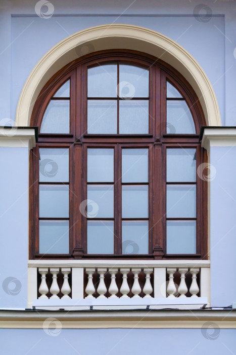 Скачать Крупный план арочного окна с деревянной рамой и декоративной белой оградой внизу на фасаде синего старинного здания фотосток Ozero