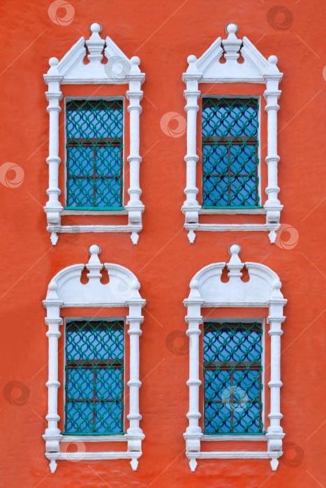 Скачать Вид крупным планом на фасад старинного красного здания с четырьмя окнами с резными наличниками из белого камня в качестве текстуры (вертикальная ориентация) фотосток Ozero