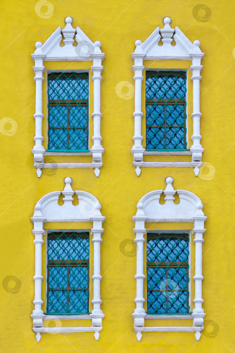 Скачать Вид спереди на фасад старинного желтого здания с четырьмя окнами с резными наличниками из белого камня в качестве текстуры (вертикальная ориентация) фотосток Ozero