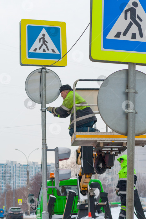 Скачать Москва, Россия, декабрь 2018 года. Рабочие в желтой униформе устанавливают дорожный знак на столбе. (редакционная статья). фотосток Ozero