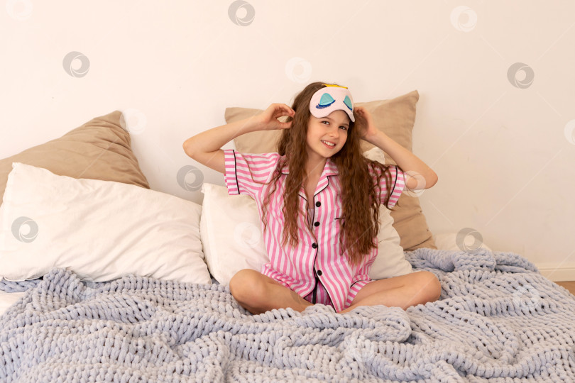 Скачать Девушка поправляет маску для сна, сидя на кровати. фотосток Ozero