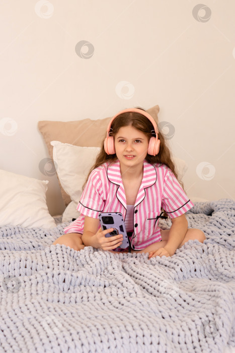 Скачать Молодая девушка в наушниках пользуется смартфоном на кровати. фотосток Ozero
