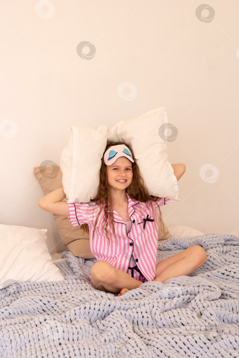 Скачать Молодая девушка сидит на кровати с подушкой и радостно смеется. фотосток Ozero