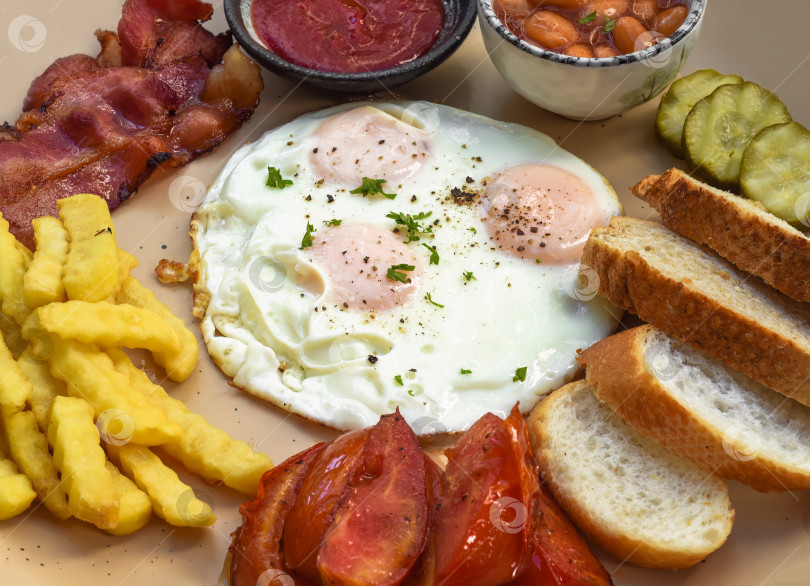 Скачать Полезный английский завтрак с яичницей-глазуньей, беконом, картофелем фри, фасолью и помидорами крупным планом фотосток Ozero