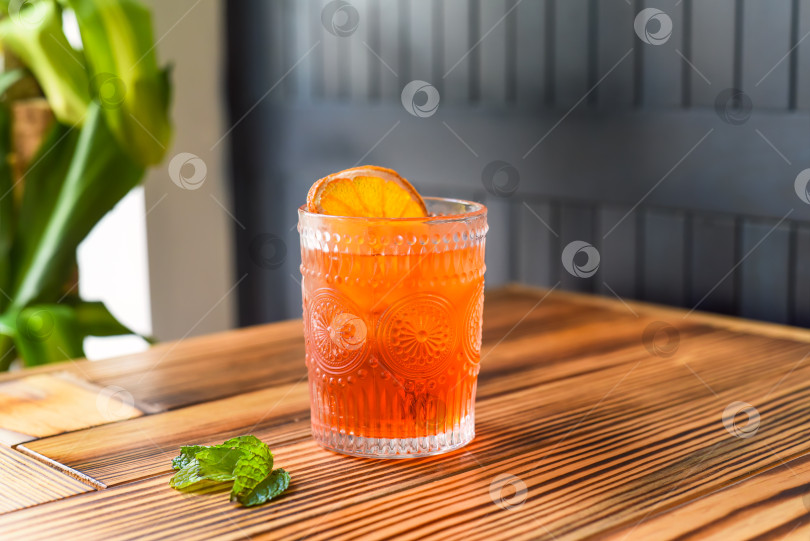 Скачать Алкогольный коктейль "Апероль Спритц" с кусочком апельсина на деревянном столе на фоне темной стены с пространством для копирования фотосток Ozero