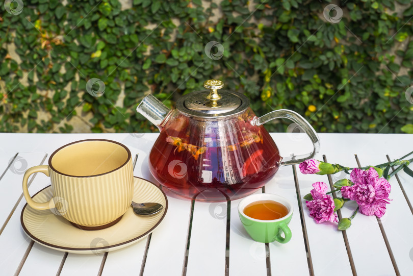 Скачать Цветочный чайник с чашкой и медом, цветы на белом деревянном столе на фоне зеленых листьев фотосток Ozero