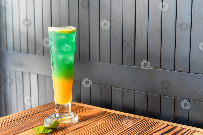 Скачать Радужный желто-зеленый алкогольный коктейль на деревянном столе на фоне темной стены с пространством для копирования фотосток Ozero