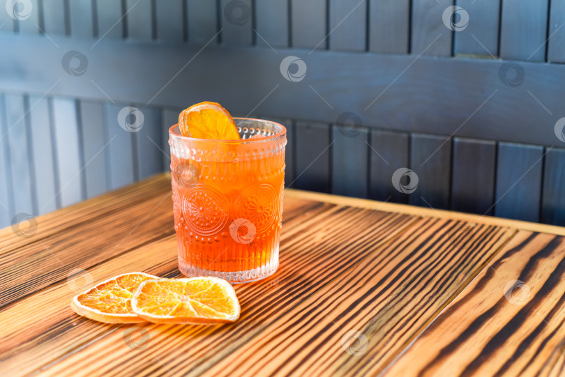 Скачать Алкогольный коктейль "Апероль Спритц" с кусочком апельсина на деревянном столе на фоне темной стены с пространством для копирования фотосток Ozero