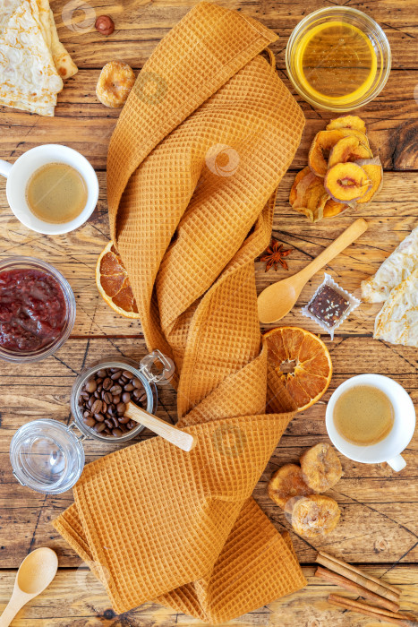 Скачать Сложенное кухонное полотенце, на котором разложены блинчики, фруктовые чипсы, орехи, мед и две чашки кофе фотосток Ozero