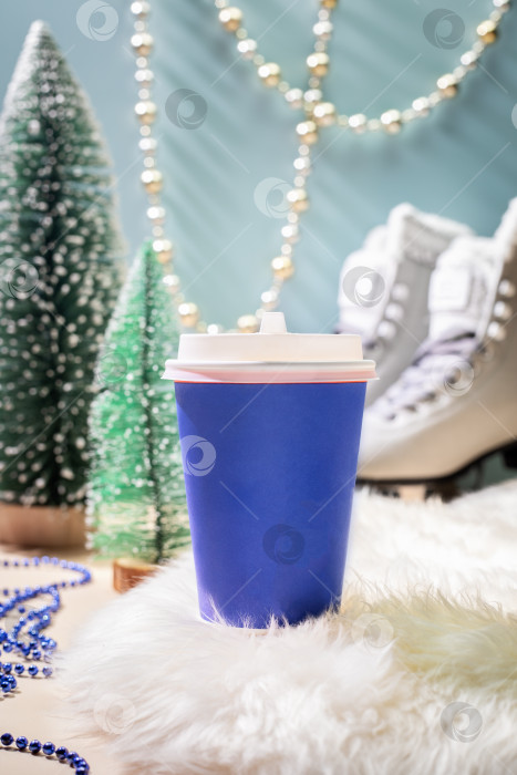 Скачать Одноразовая синяя чашка для кофе на белом меховом коврике с новогодним декором и коньками фотосток Ozero
