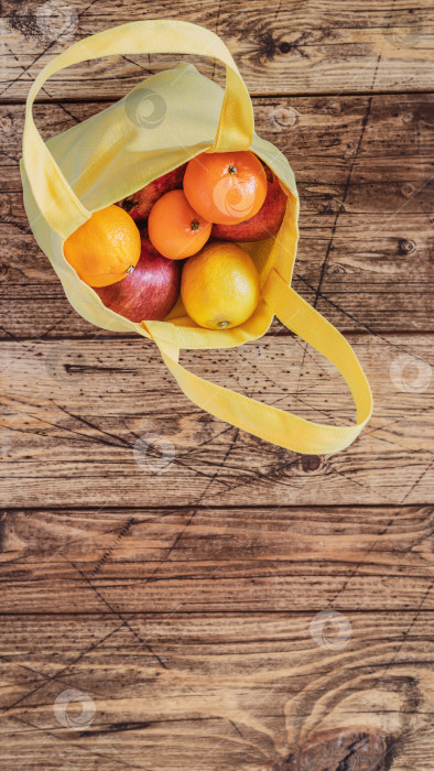 Скачать Натуральные фрукты: лимоны, апельсины, грейпфруты и гранаты в желтом хлопчатобумажном пакете на деревянном фоне. фотосток Ozero