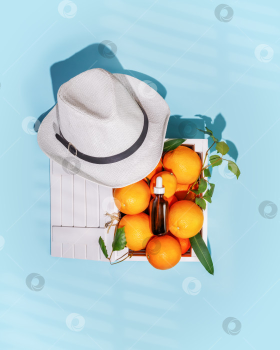 Скачать Цитрусовые в деревянной коробке, бутылка апельсиновой сыворотки и летняя шляпа на синем фоне фотосток Ozero