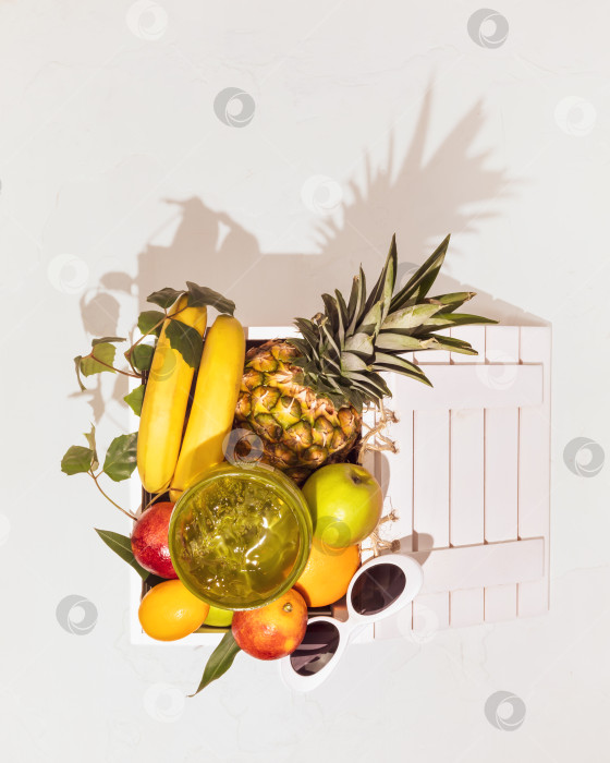 Скачать Свежие, спелые тропические фрукты с листьями в деревянной коробке, косметический увлажняющий гель для тела и солнцезащитные очки фотосток Ozero