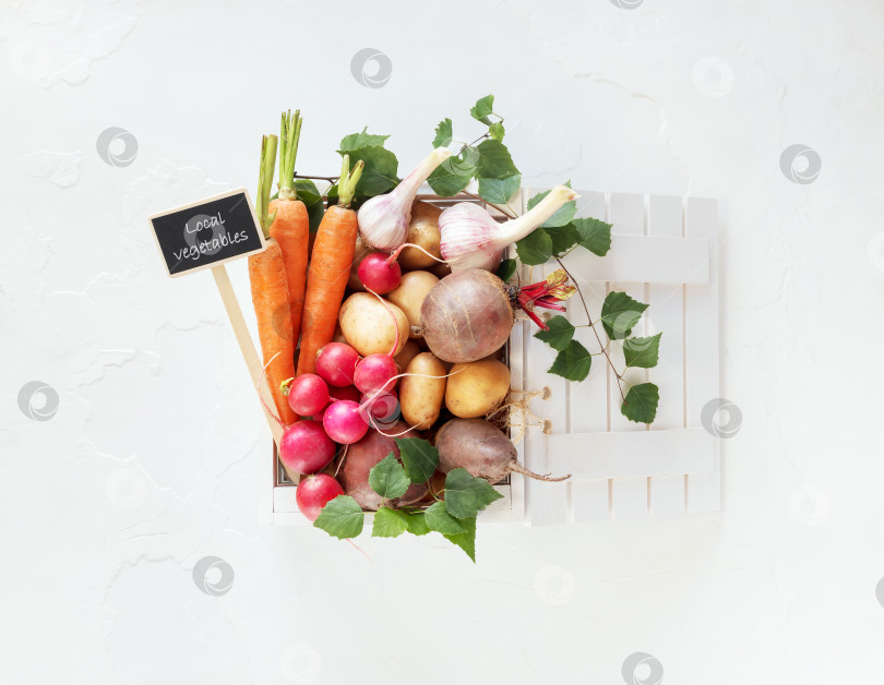 Скачать Деревянная коробка, полная свежих органических овощей с местного рынка, на белом столе фотосток Ozero