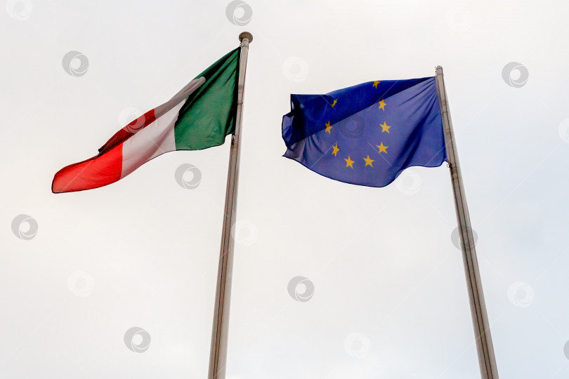 Скачать Вид флагов Италии, Европейского Союза на фоне облачного неба фотосток Ozero