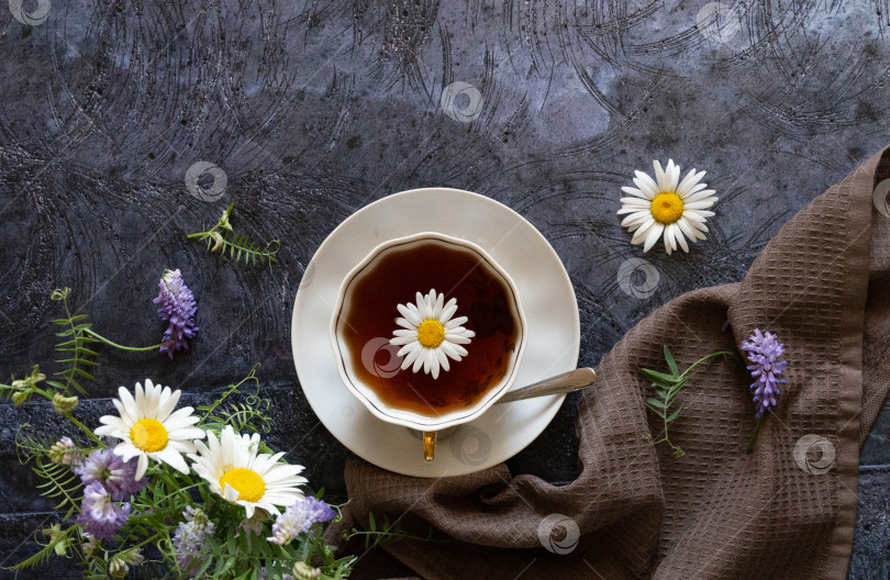 Скачать Травяной ромашковый чай и цветы ромашки рядом с чайником и чайным стаканом. На фоне сельской местности. фотосток Ozero