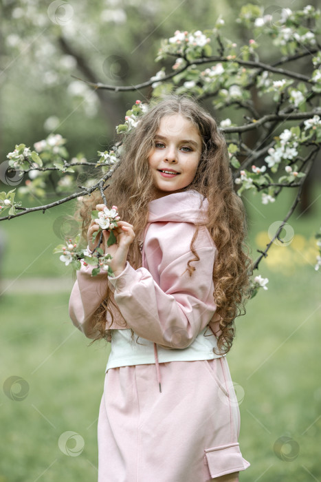 Скачать Красивая маленькая девочка в розовом платье стоит у цветущей белой яблони в парке и наслаждается красотой цветущего сада, весной фотосток Ozero