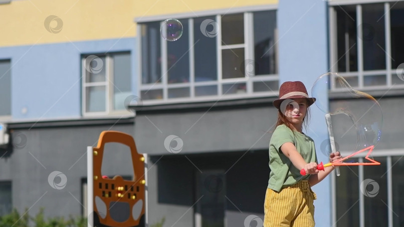 Скачать Симпатичная девочка школьного возраста пускает большие мыльные пузыри во дворе многоэтажного дома фотосток Ozero