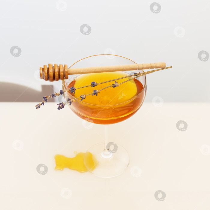 Скачать Золотистый жидкий мед в стеклянном бокале, веточки лаванды и ковшик для меда на белом столе фотосток Ozero