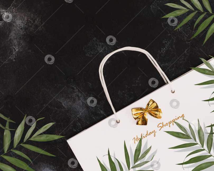 Скачать Подарочный белый пакет с пальмовыми листьями и праздничным декором на черном текстурном фоне с пространством для текста фотосток Ozero