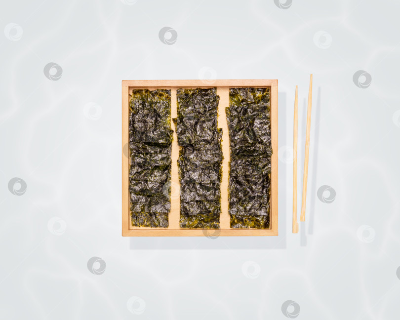 Скачать Закуска из органических сушеных морских водорослей на деревянной доске и палочках для еды на синем фоне фотосток Ozero