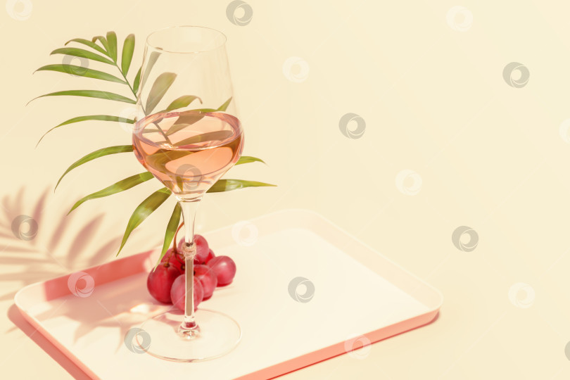 Скачать Бокал розового вина с пальмовыми листьями и виноградом на розовом фоне фотосток Ozero