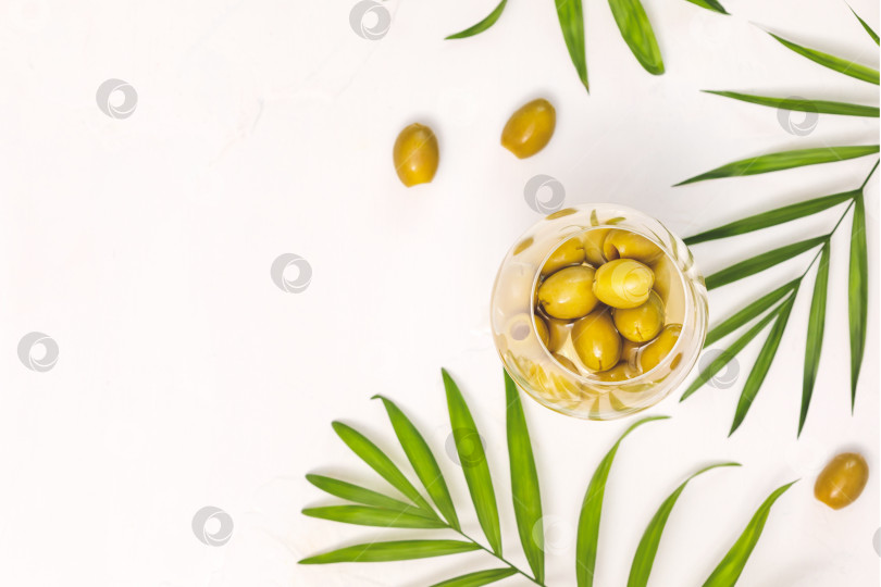 Скачать Зеленые оливки в бокале и пальмовые листья на белом фоне фотосток Ozero