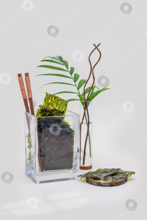 Скачать Органическая закуска из морских водорослей нори в стеклянной банке с палочками для еды и пальмовыми листьями на синем фоне фотосток Ozero