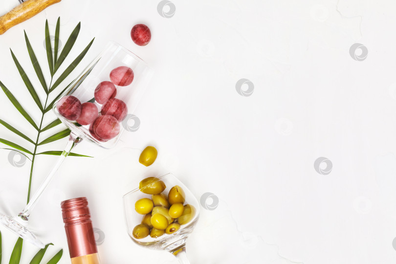 Скачать Бокалы для вина с виноградом и зелеными оливками, бутылка розового вина и пальмовые листья фотосток Ozero
