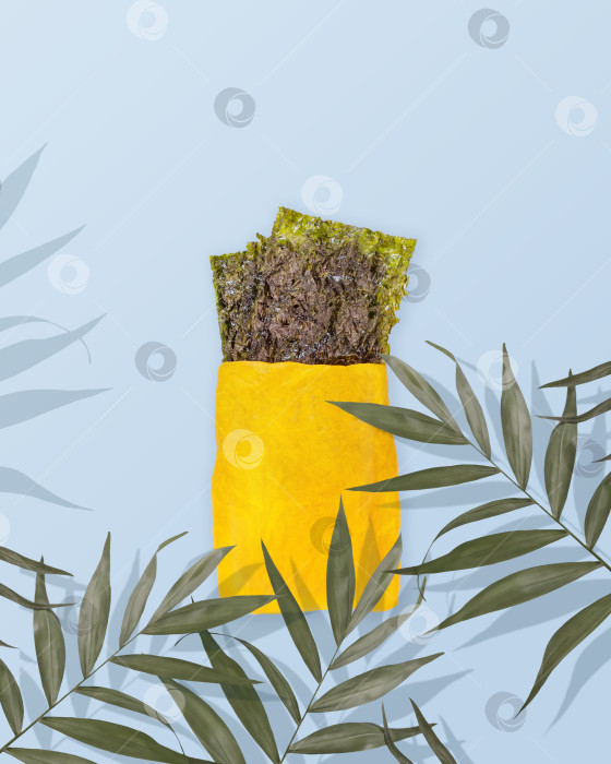 Скачать Закуска из соленых сушеных морских водорослей в желтом бумажном пакете с пальмовыми листьями на синем фоне фотосток Ozero