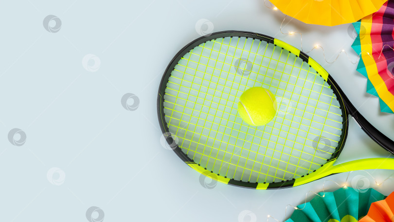 Скачать Теннисная ракетка, желтый теннисный мяч, разноцветные бумажные веера и световая гирлянда на синем фоне фотосток Ozero