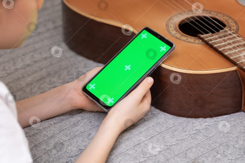 Скачать Мальчик с гитарой держит в руках смартфон с зеленым экраном фотосток Ozero