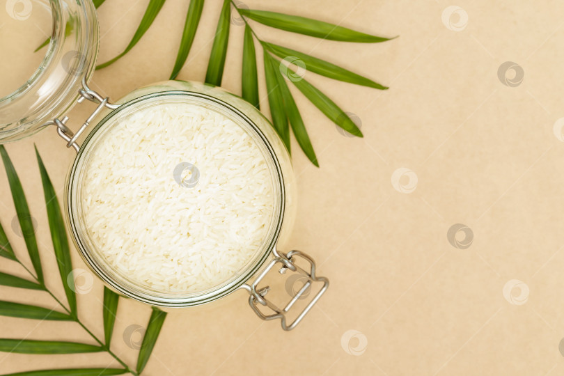 Скачать Рисовые зерна в стеклянной миске и пальмовые листья на фоне поделок фотосток Ozero