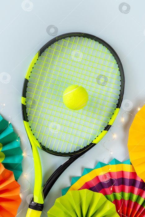 Скачать Теннисная ракетка, желтый теннисный мяч, разноцветные бумажные веера и световая гирлянда на синем фоне фотосток Ozero