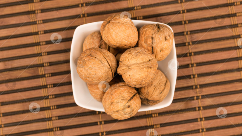 Скачать Горка грецких орехов в тарелке, стоящей на бамбуковой циновке. фотосток Ozero