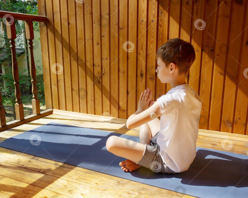 Скачать Мальчик с диабетическим сенсором сидит на гимнастическом коврике в позе йоги фотосток Ozero