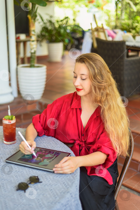 Скачать Красивая блондинка, художница и иллюстратор, придумала концепцию своего рисунка, сидя за столом с электронным планшетом и стилусом фотосток Ozero