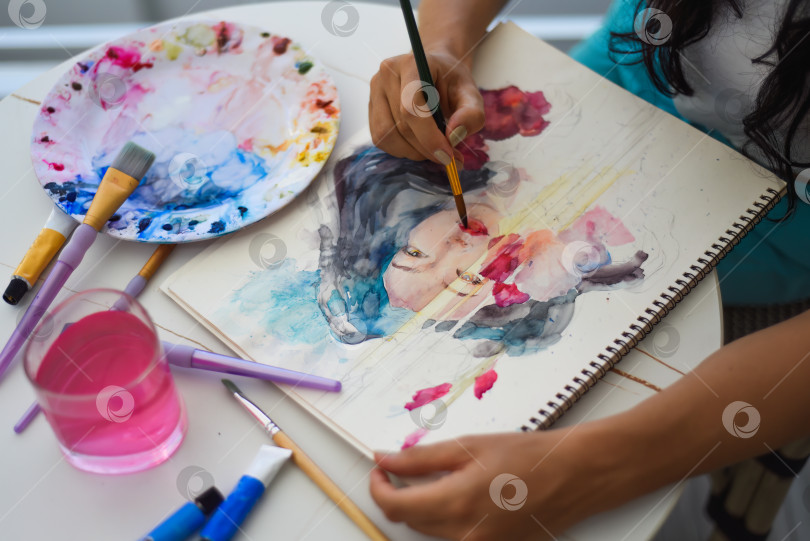 Скачать Женщина рисует акварелью рисунок азиатской девушки кистью на столе с водой и красками фотосток Ozero