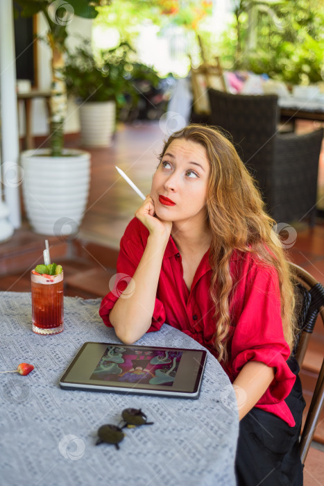 Скачать Красивая блондинка, художница и иллюстратор, придумала концепцию своего рисунка, сидя за столом с электронным планшетом и стилусом фотосток Ozero
